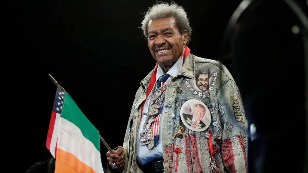 Don King in his flamboyant USA-themed outfit, holding an Irish flag in one hand and an American flag in the other, showcasing his distinctive promotional style.