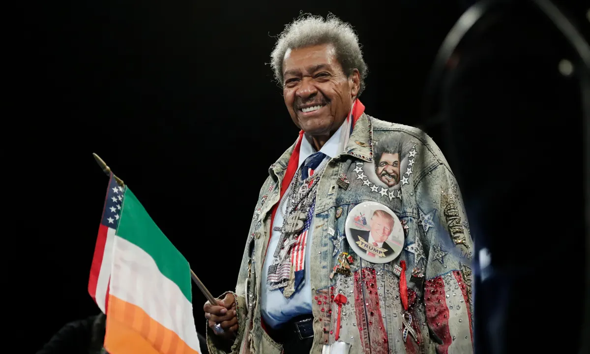 Don King in his flamboyant USA-themed outfit, holding an Irish flag in one hand and an American flag in the other, showcasing his distinctive promotional style.