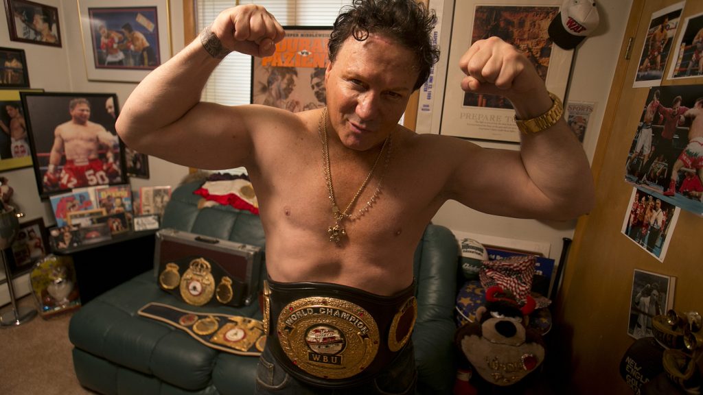 Vinny Pazienza proudly displaying his WBU World Championship belt in his living room, smiling broadly.