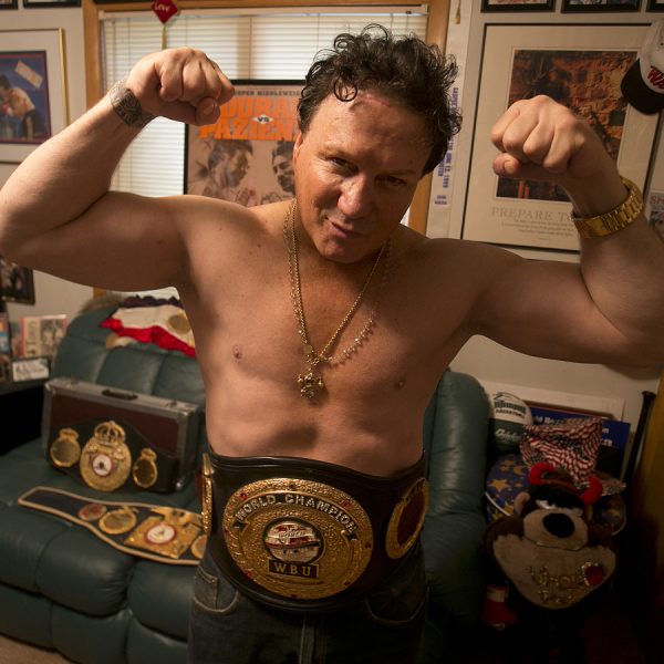 Vinny Pazienza proudly displaying his WBU World Championship belt in his living room, smiling broadly.